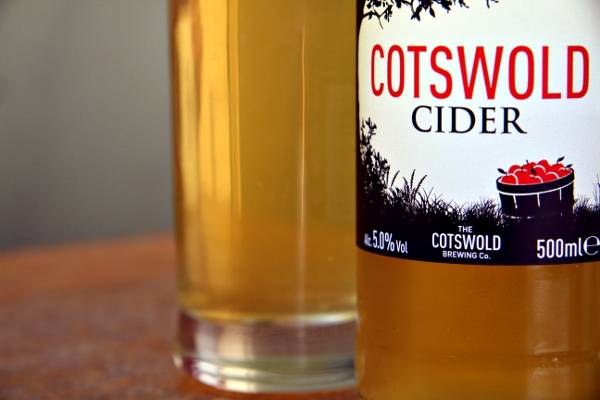 bottle of cotswold cider sitting on the table with a glass next to it