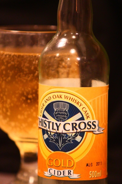 Thistly Cross Gold whisky cider, shot of bottle with glass in background. Yum.